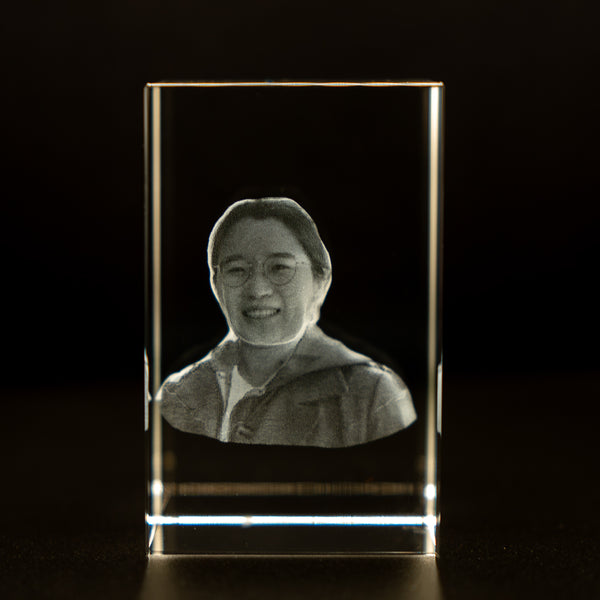 A custom 3D crystal engraving of a woman's face illuminated from the inside with LED light, placed against a dark background.