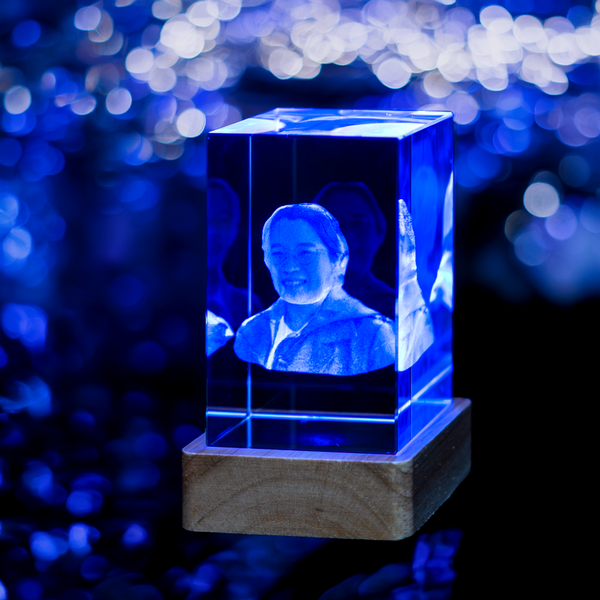 A custom 3D crystal engraving of a woman's portrait illuminated with blue light, mounted on a wooden base.